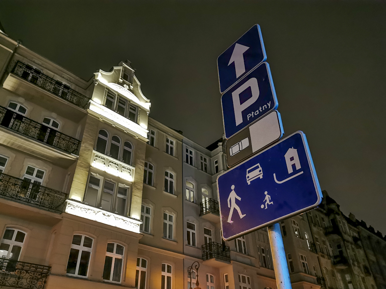 Poznań nocą: ulica Wielka. Na słupku wisi kilka znaków, w tym oznajmiający wjazd do strefy zamieszkania